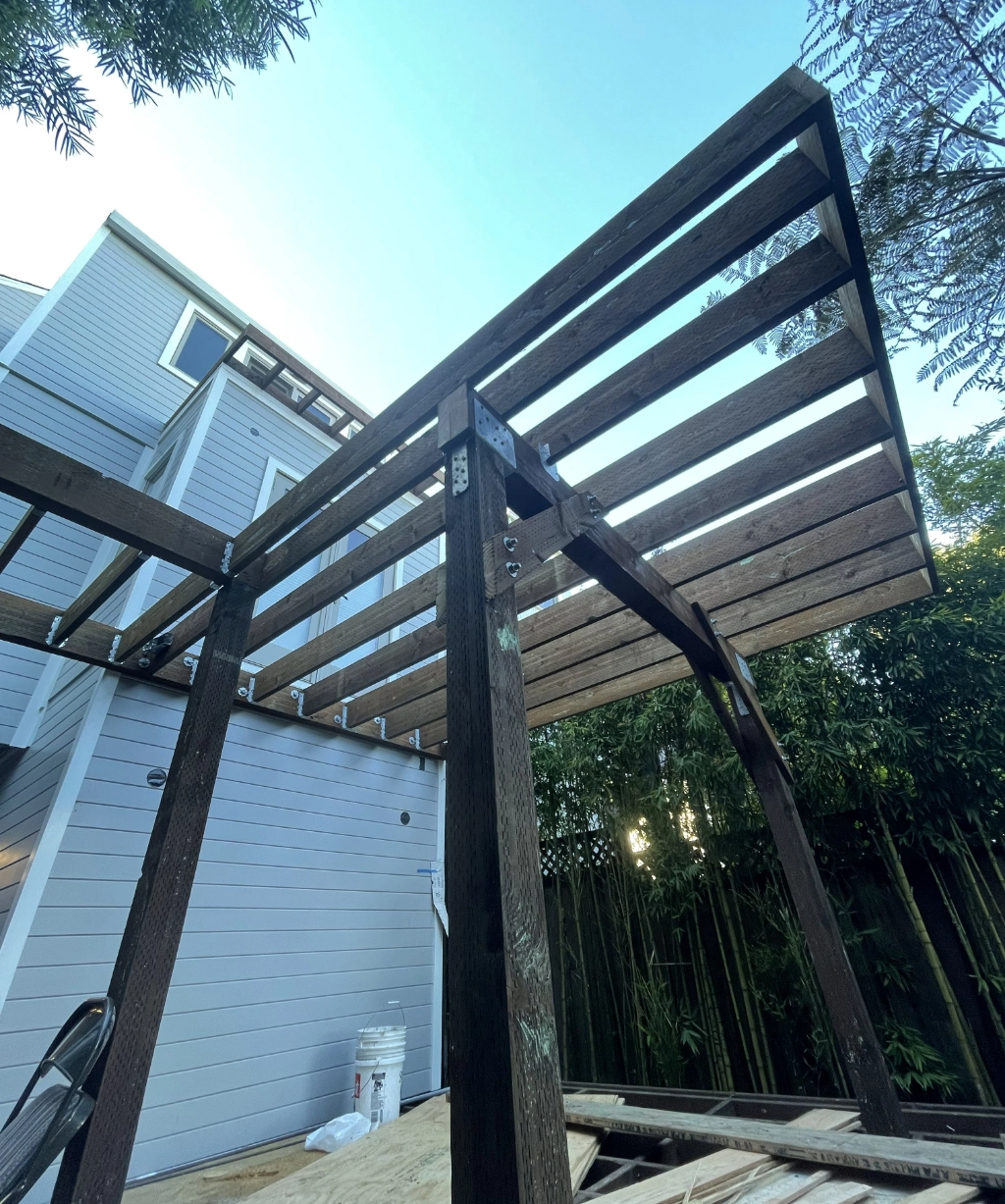 A wooden pergola frame is under construction next to a modern house.