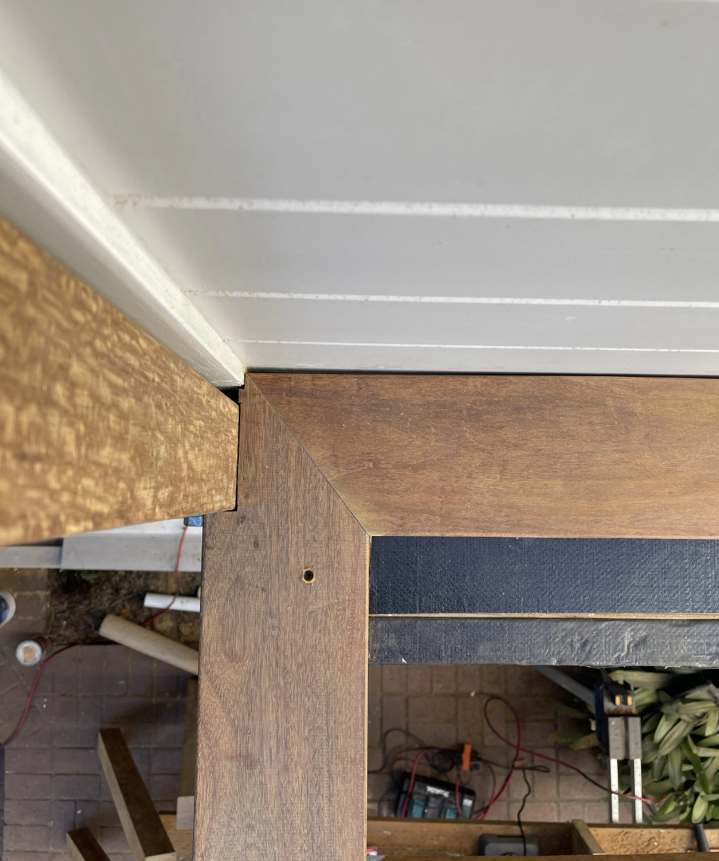 Close-up view of a wooden frame construction with neatly aligned wooden beams. Tools and materials are visible on the ground below.