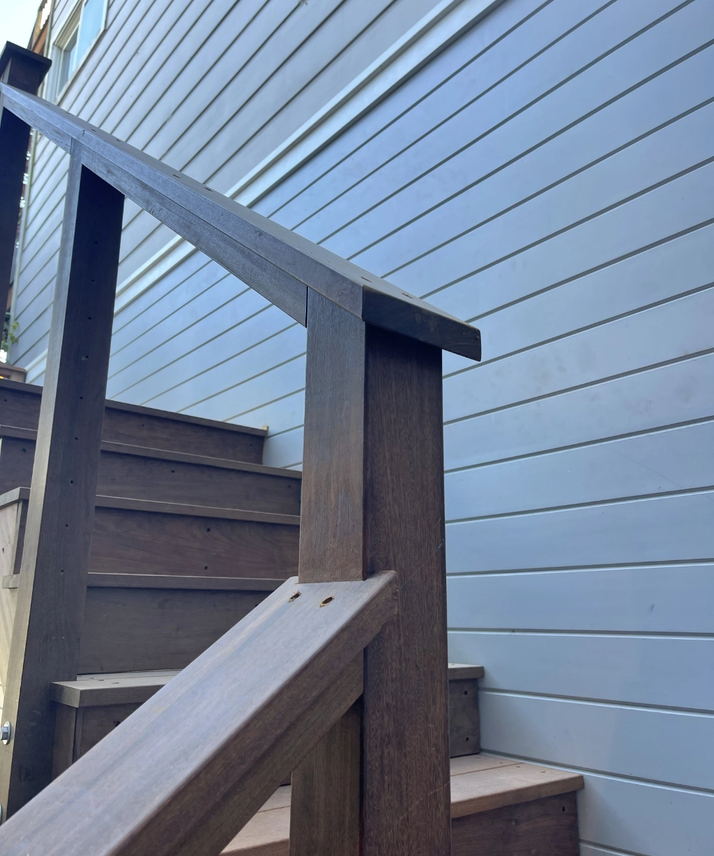 Wooden stairs with a handrail lead up alongside the blue-paneled exterior wall, offering a charming ascent in a picturesque setting.