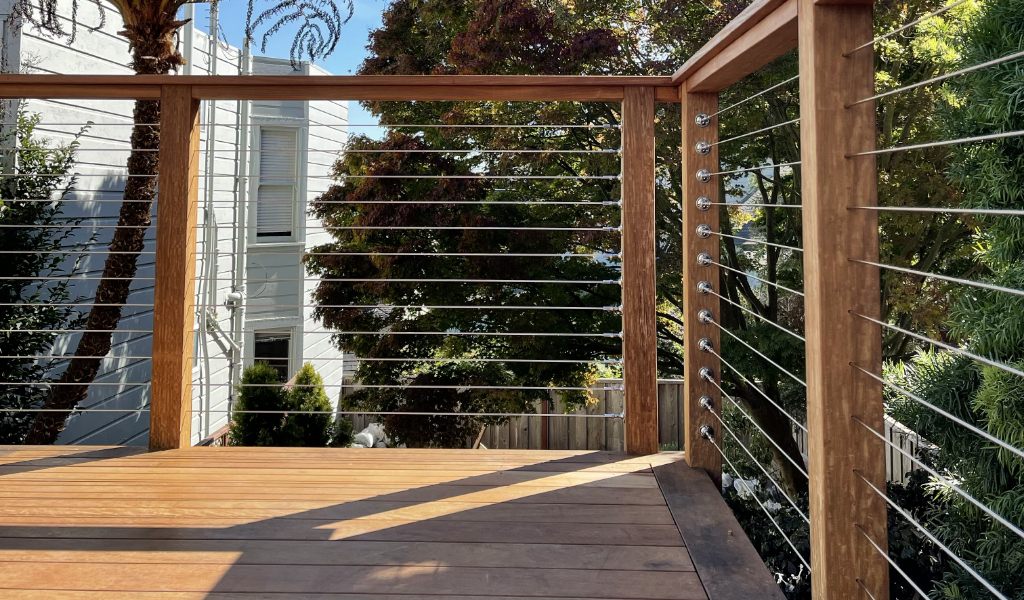 This wooden deck with a sleek metal railing offers a serene escape surrounded by trees, adjoining a pristine white building.