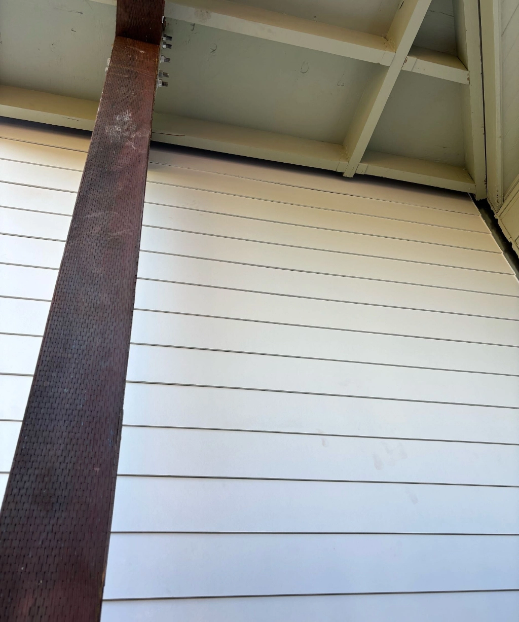 A wooden ceiling with a large, vertical rusty metal beam and horizontal white wall panels.