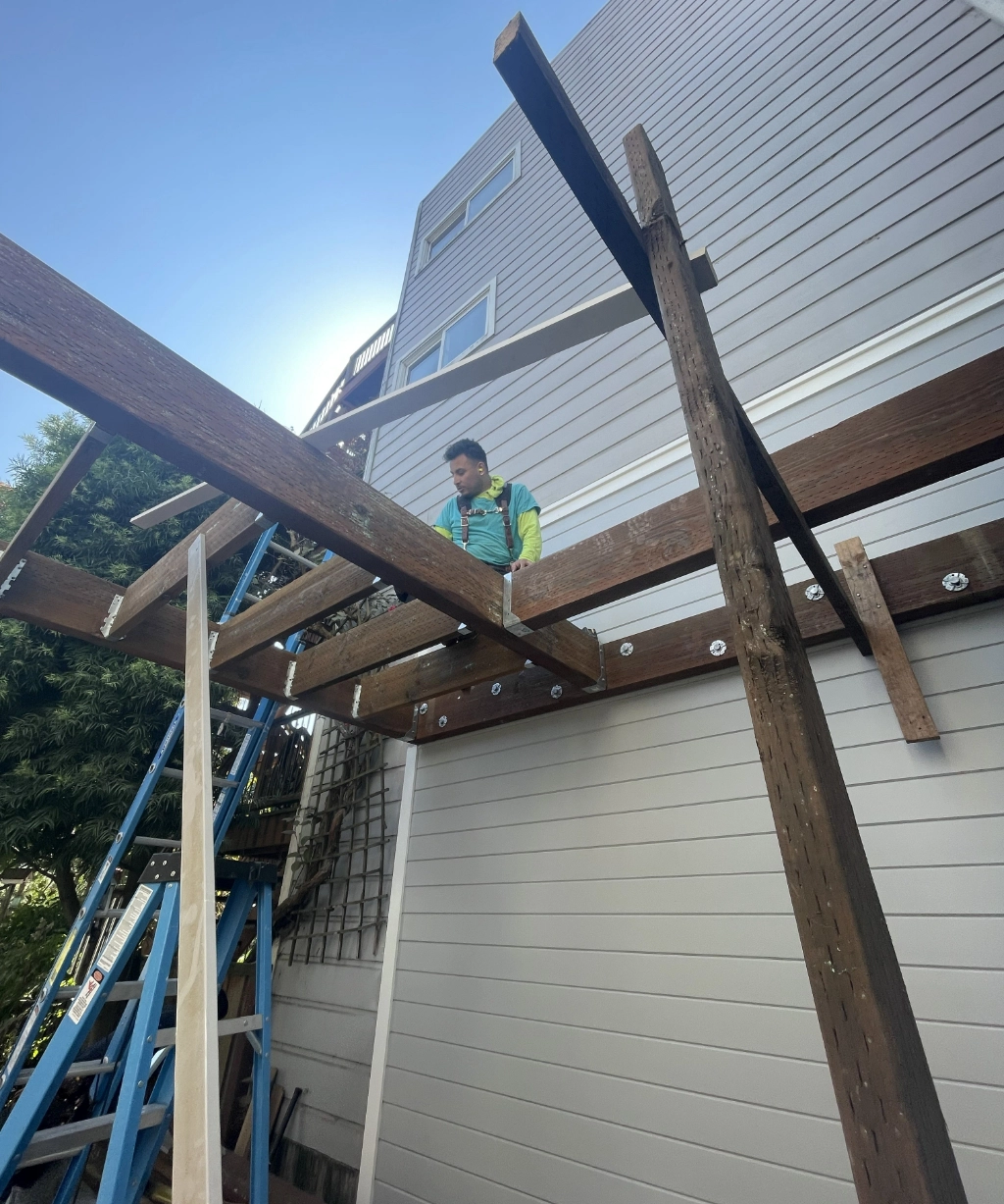 A person stands on a wooden structure under construction beside a building. A ladder leans nearby under the clear sky, symbolizing progress and new beginnings.