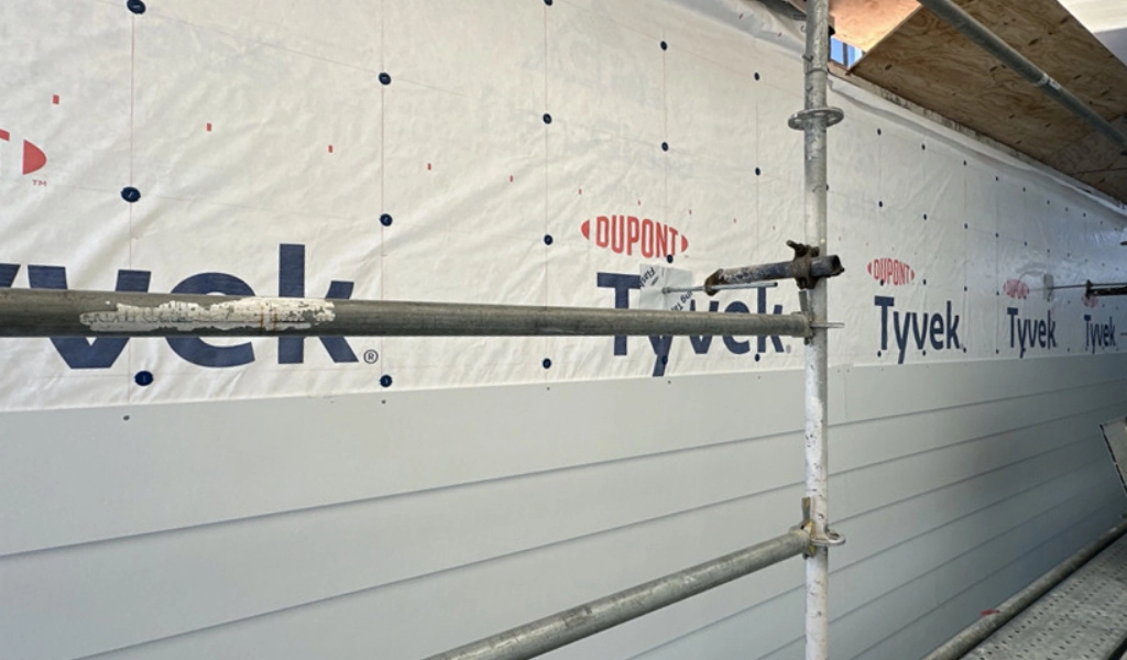 Scaffolding stands in front of a building wall, enveloped in DuPont Tyvek sheeting.