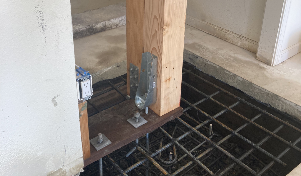 At a construction site, a wooden beam is securely attached to a metal bracket over exposed rebar, seamlessly blending strength and precision.