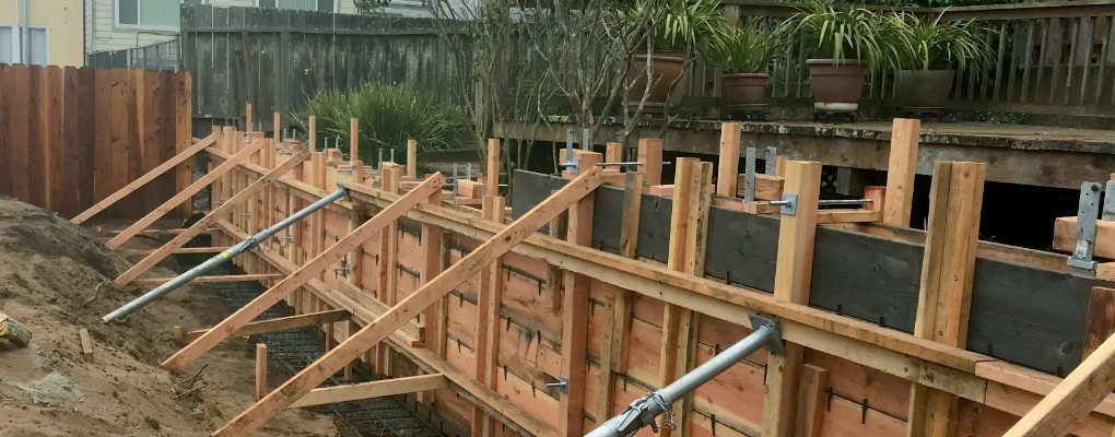 Matthew Kelly Construction presents a backyard transformation, showcasing the wooden framework for a retaining wall. Metal support rods reinforce the structure, reflecting our commitment to quality and durability in every project.